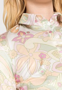 Primer plano de una camisa de cuello con patrones florales y abstractos en tonos pasteles de rosa, verde y beige sobre una tela clara.