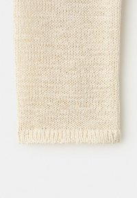 Tissu tricoté couleur crème avec ourlet côtelé, montrant un matériau doux et texturé en mélange de laine ou de coton.