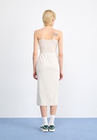 Light beige ribbed midi dress with thin straps, fitted waist, and flared hem. Paired with white socks and green-accented sneakers.