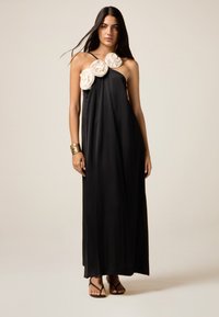 Schwarzes, bodenlanges Kleid mit asymmetrischem Design und großen elfenbeinfarbenen Blumenakzenten an einer Schulter; glattes, leichtes Material; dünne Träger.