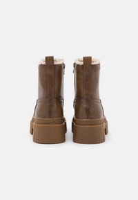 Brązowe skórzane botki za kostkę, z puszystym białym wyściółką, masywną brązową podeszwą oraz zapięciem na zamek z tyłu. Widoczne detale tekstury.