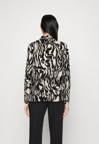 Blusa de manga larga negra y beige con un patrón abstracto en espiral, con un cuello tipo chal y una tela suave. Combinada con pantalones negros.