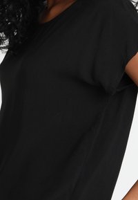 Haut noir, ample, à manches courtes. Tissu doux, encolure ronde, coutures minimales, sans motifs ni ornements visibles.