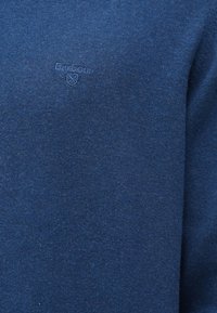 Μπλε πλεχτό πουλόβερ με υφή υφάσματος. Διαθέτει ένα μικρό ανάγλυφο λογότυπο στο στήθος. Απλός σχεδιασμός, στρογγυλή λαιμόκοψη και μακριά μανίκια.