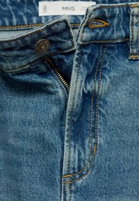 Vorderansicht von blauen Jeans mit teilweise geöffnetem Reißverschluss, Metallknopf und sichtbaren orangefarbenen Nähten am Bund.