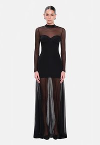 Abito nero con maniche lunghe in rete trasparente, corpetto aderente con scollo a cuore e gonna fluente in tessuto trasparente.