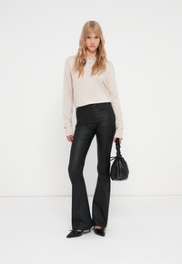 Bež košulja dugih rukava s ovratnikom i detaljima od dugmadi, u kombinaciji s crnim kožnim hlačama s iskrivljenim nogavicama. Crna torba s naboranim dizajnom.