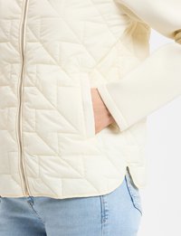 Helle, gesteppte Jacke mit Reißverschluss, diagonal genäht, mit zwei Seitentaschen und kontrastierenden strukturierten Ärmeln.