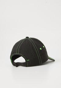 Zwarte pet met groene stiksels en oogjes, met een gebogen klep en een verstelbare band aan de achterkant. Textuurstof met een lichte glans.