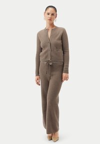 Beige stickat lounge-set med en texturerad kofta med knappar, en ficka och matchande byxor med dragsko i midjan och avslappnad passform.