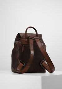 Brun läderryggsäck med en strukturerad design, utrustad med justerbara remmar, ett handtag på toppen och en dragkedjefrontficka. Texturerade detaljer ingår.