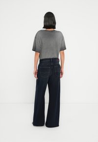 Γκρι υπερμεγέθη μπλούζα και σκούρο τζιν παντελόνι με φαρδύ πόδι. Η μπλούζα έχει άνετη γραμμή με ριγωτά μανίκια· το τζ ιν διαθέτει ραμμένες τσέπες και ψηλή μέση.