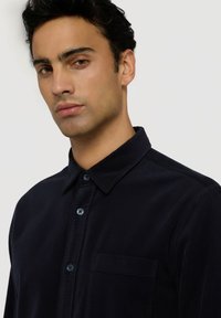 Námořnická manšestrová košile s límečkem, předním zapínáním na knoflíky a detailem kapsy. Textura má vertikální žebra.