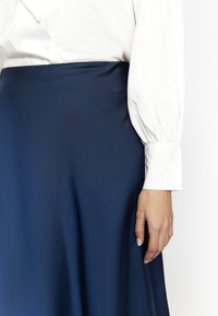 Mørkeblå satin nederdel med en glat overflade, parret med en hvid bluse med voluminøse ærmer og knapdetaljer.