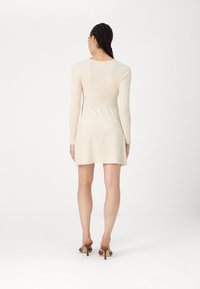 Robe-pull côtelée jusqu'aux genoux, de couleur beige clair, avec des manches longues et un col arrondi, dotée d'un ourlet évasé et de détails minimalistes.