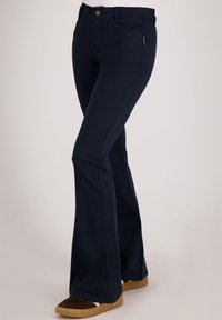 Donkerblauwe flare-broek gemaakt van een katoenmix, met een voorzak, knoopsluiting en subtiele branding aan de zijkant.