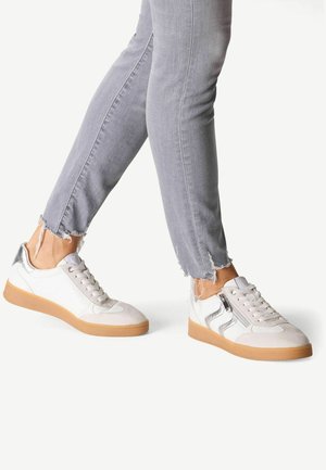 White and silver sneakers with a gum sole, featuring a textured upper, lace closure, and decorative side zipper detail. Worn with frayed gray jeans.