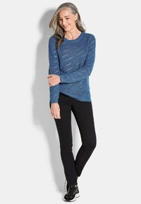 Blauer Strickpullover mit strukturiertem Muster, rundem Ausschnitt und langen Ärmeln, kombiniert mit schwarzen Slim-Fit-Hosen und schwarzen Sneakern.