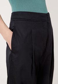 Svarta byxor med en slät yta, veck vid midjan och sidofickor. Tillsammans med en figurnära, ribbad top i teal.