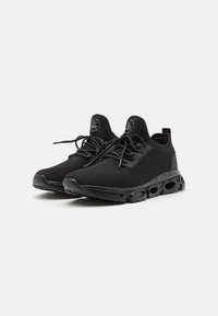 Zapatillas deportivas negras con parte superior de malla, cuello acolchado, suela texturizada con bolsas de aire y cordones planos para un ajuste seguro.