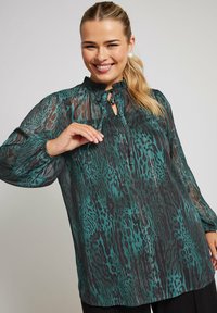 Blusa trasparente in teal con motivo leopardato, colletto alla mandarino e chiusura a fiocco, dotata di maniche lunghe e dettagli testurizzati.