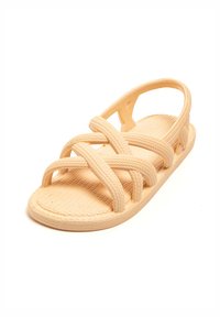 Beige sandal made of textured material, featuring crisscross straps, an open heel design, and a flat sole with subtle detailing.