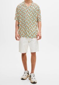 Multicolored short-sleeve shirt with geometric pattern in shades of blue, orange, and green, paired with white shorts and chunky sneakers.