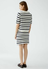 Strickzweisitzer bestehend aus Marineblau- und weißen Streifen, kurzärmligem Oberteil, tailliertem Rock und Wellensaum-Details. Braune Schuhe runden den Look ab.