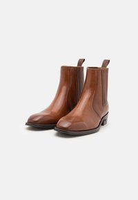 Botas de tobillo de cuero marrón con paneles laterales elásticos, puntera cuadrada, textura suave y tirador en la parte posterior para facilitar el uso.
