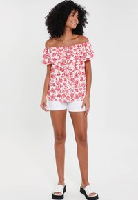 Top floreale bianco con fiori rossi, con maniche a volant. Abbinato a pantaloni corti bianchi e sandali platform neri.