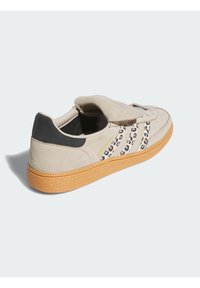 Bež suède tenisice s crnim naglaskom na peti, s prugama životinjskog uzorka i teksturiranom gumenom potplatom. Vezivanje na čičak na vrhu.