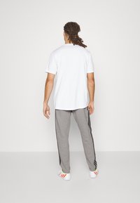 Vit bomulls-t-shirt med korta ärmar, parat med grå sweatpants med svarta sidostripes och färgade detaljer på skorna.