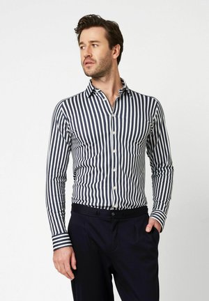 Blau-weiß gestreiftes Langarmhemd mit einem geknöpften Kragen, das eine taillierte Passform und kontrastierende Manschetten aufweist. Kombiniert mit einer dunklen Hose.