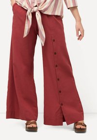 Pantalons larges rouges en tissu léger, avec des boutons sur les côtés et un design fendu. Associés à un haut rayé noué.