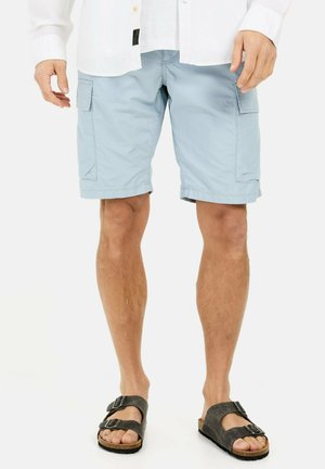Lichtblauwe cargo shorts met zijzakken, gemaakt van zacht materiaal, met opgerolde zoom. Gecombineerd met donkere sandalen met banden en gespen.