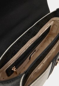 Sac à main en cuir noir avec fermeture éclair, doté d'un intérieur avec un revêtement à motifs beige et noir, et plusieurs compartiments, y compris une poche zippée.