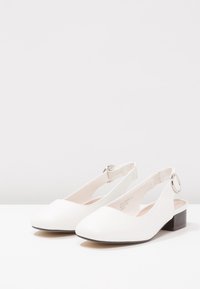 Bottines blanches à talon bas avec un embout arrondi, à brides avec boucle réglable en ton argenté. Fabriquées en matériau lisse ressemblant à du cuir.