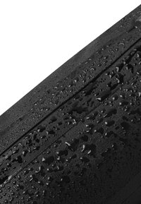 Czarna wodoodporna powierzchnia o teksturowanym wykończeniu, z kroplami wody i widocznymi wzorami. Materiał wygląda na trwały i odporny na warunki atmosferyczne.