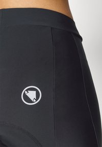 Crne atletske kratke hlače izrađene od glatkog, rastezljivog materijala. Sadrže logo u kružnom dizajnu na donjoj strani i širok elastični pojas.