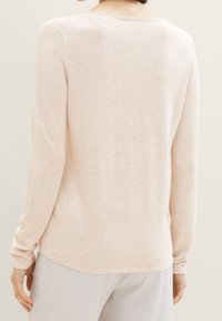 Heller rosa langärmliger Pullover aus weichem Material, mit rundem Halsausschnitt und gerippten Bündchen. Nahtdetails verlaufen entlang der Schultern.