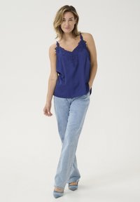 Mornarsko modra top z čipkastimi detajli ob vratnem izrezu, v kombinaciji s svetlomodrimi črkami in modrimi salonarji s špicasto konico.