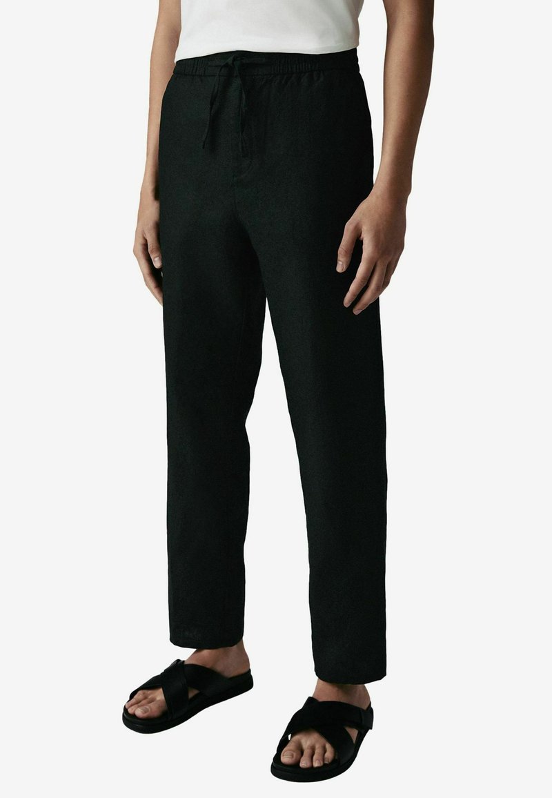 Pantaloni din in negri cu talie elastică și șnur de legare, având un croi lejer și design cu picior drept, asortați cu sandale negre.