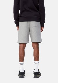 Gray cotton shorts featuring a back pocket, paired with white socks and black athletic shoes. Model stands facing away on a neutral background.
