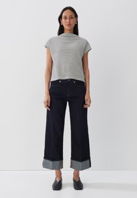 Top a righe, a maniche corte, bianco e nero, abbinato a jeans in denim scuro a gamba larga con risvolti in tessuto grigio a contrasto. Scarpe nere.