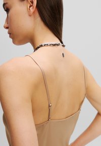 Nude tanktop met dunne banden, voorzien van een metalen chain accent op de achterkant met een sluitingdetail en een zilveren kettingverlenging.