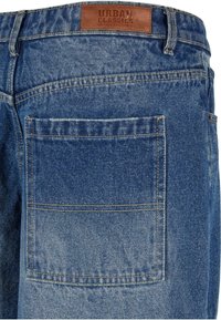 Denim jeans in a light blue wash, featuring a leather tag labeled "URBAN CLASSICS," with visible stitching and a back pocket design.
