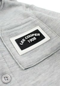 Sweat à capuche gris avec un patch en caoutchouc noir et blanc marqué "LEE COOPER 1908" sur la poitrine gauche ; texture lisse avec fermeture à boutons.