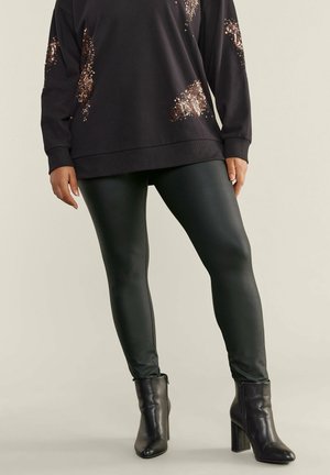 Sweatshirt noir avec des accents en sequins, associé à des leggings verts brillants et des bottines. Le sweatshirt a une coupe décontractée et des manches longues.