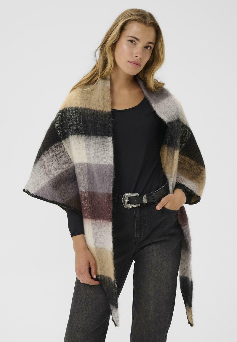 Plaid wrap made of soft wool, featuring stripes in beige, black, and gray. Hem is scalloped. Paired with a black top and jeans.