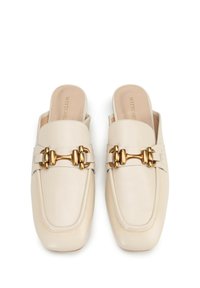Mule in pelle beige con punta quadrata, dettagli in metallo dorato, texture liscia e design slip-on. Nome del marchio impresso sulle sole interne.